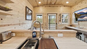 Interior de madera con cocina, que incluye un lavamanos, un tostador y una ventana con vistas a la montaña.