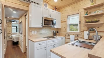 A modern kitchen with white cabinets, a stainless steel microwave, and a wooden countertop.