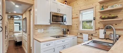 A modern kitchen with white cabinets, a stainless steel microwave, and a wooden countertop.