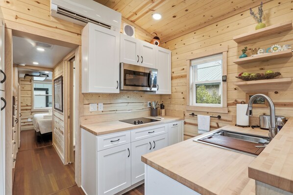 A modern kitchen with white cabinets, a stainless steel microwave, and a wooden countertop.