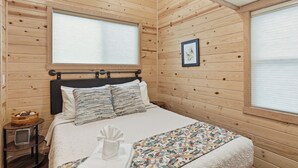 A wooden-paneled room with a bed, a small bedside table, and a window with blinds. - Chama Crossing - Tiny Train Next to Railroad (Chama)