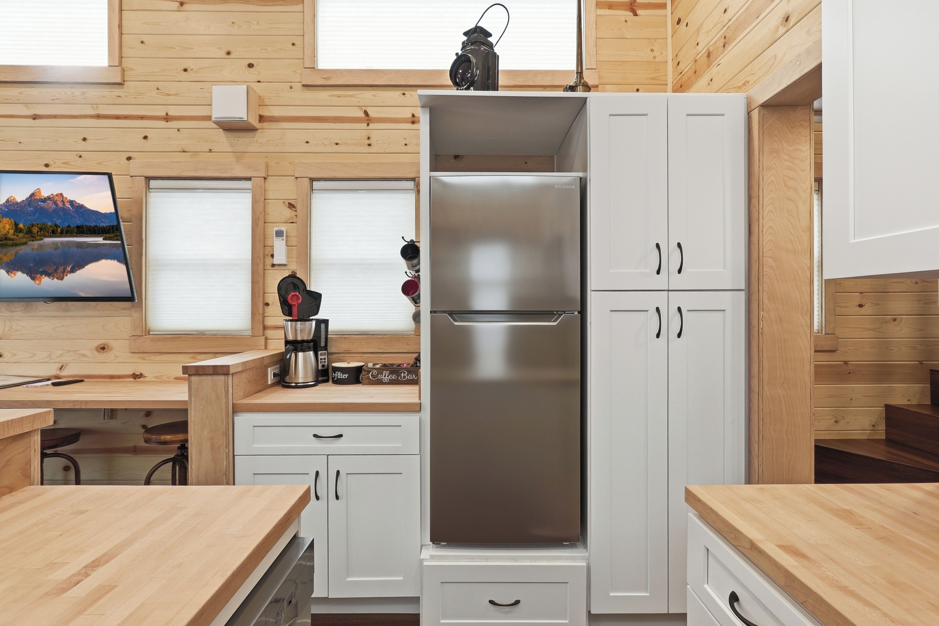 A modern kitchen with wooden walls, a stainless steel refrigerator, and a coffee machine.