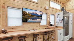 A wooden interior with a kitchen area, bar stools, and a large flat-screen TV mounted on the wall. - Chama Crossing - Tiny Train Next to Railroad (Chama)