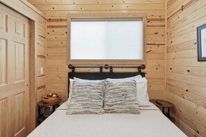 Una habitación con paneles de madera, una cama, un ventanal y una puerta de madera.