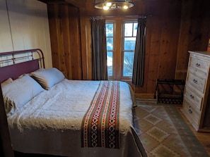 A wooden room with a bed, a dresser, and a window with curtains.