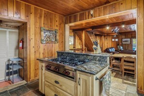 A wooden interior with a kitchen featuring a stove, cabinets, and a dining area with a table and chairs. - Chama Crossing - Historic Home next to Railroad (Chama)
