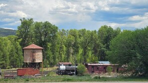 Una estación de tren rústica con una torre de señales de madera, una locomotora de vapor y un vagón de cola.