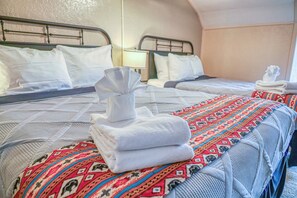 A hotel room with two beds, each with white linens and pillows, a patterned blanket, and a folded towel on the bed. - Chama Crossing - Historic Home next to Railroad (Chama)