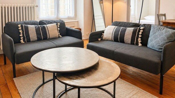 A modern living room with two sofas, a round coffee table, a floor lamp, and a large mirror. - Cosy & Welcoming Apartment – City Center – Sleeps 3/4 (Angers)