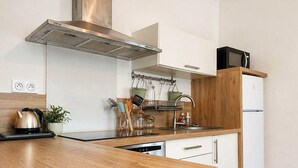 A modern kitchen with a stainless steel range hood, white cabinetry, a wooden countertop, a kettle, and a microwave. - Cosy & Welcoming Apartment – City Center – Sleeps 3/4 (Angers)