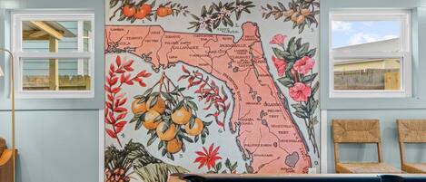 A pool table with a Florida-themed map mural, a window with a view, and two wicker chairs.