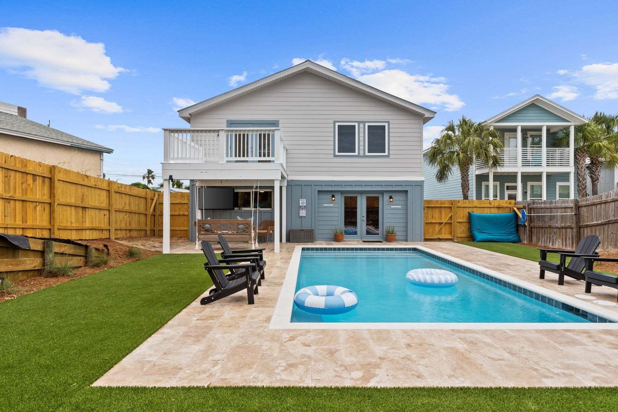 A two-story house with a backyard swimming pool, a covered patio, and a wooden fence.