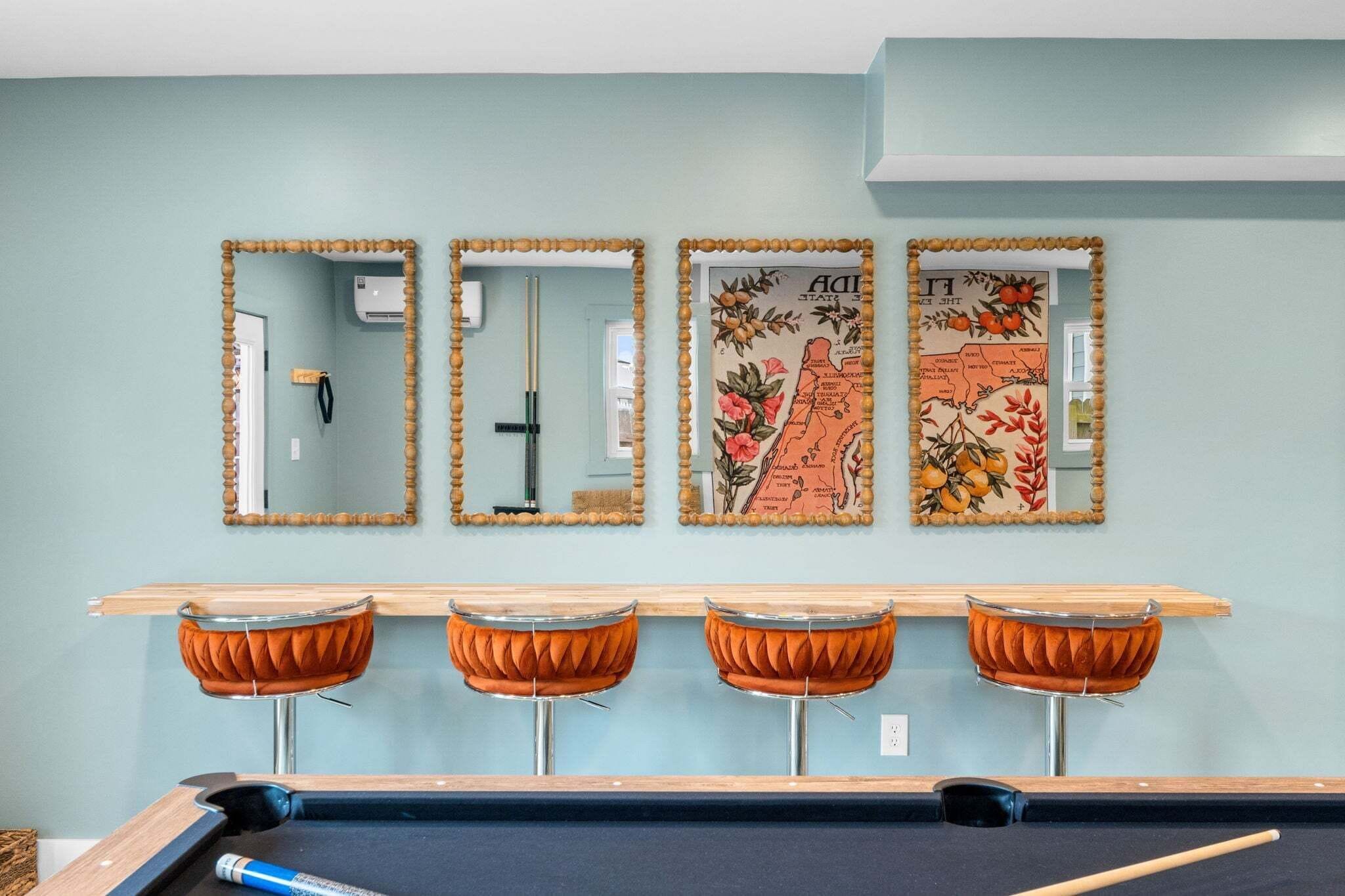 A pool table with four bar stools, three mirrors with decorative frames, and a wall with a floral map artwork.