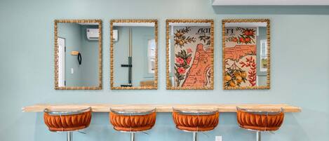 A pool table with four bar stools, three mirrors with decorative frames, and a wall with a floral map artwork.