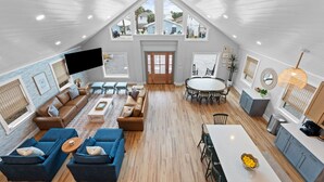 A spacious loft with a high ceiling, a dining area, a living room with sofas, and a kitchen area. - Fall Deals + Snowbird Rates | Coastal Stay Near the Beach (Panama City Beach)