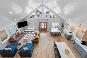 A spacious loft with a high ceiling, a dining area, a living room with sofas, and a kitchen area. - Fall Deals + Snowbird Rates | Coastal Stay Near the Beach (Panama City Beach)