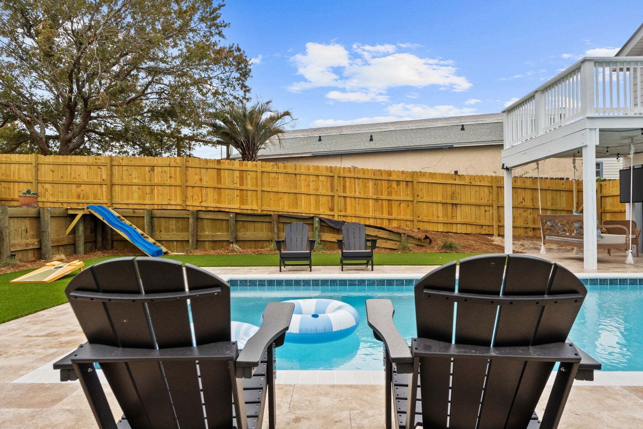 Un patio trasero con piscina, dos sillas Adirondack, un tobogán y una valla de madera.