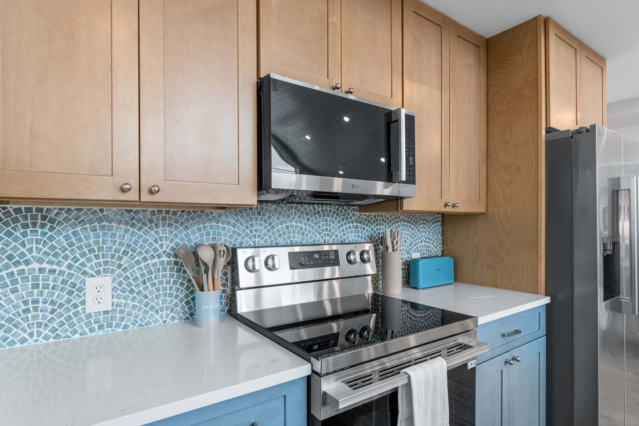 Una cocina con armarios de madera, un microondas de acero inoxidable, un horno y un refrigerador.