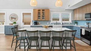 A modern kitchen with a central island, wooden cabinets, and pendant lighting. - Fall Deals + Snowbird Rates | Coastal Stay Near the Beach (Panama City Beach)