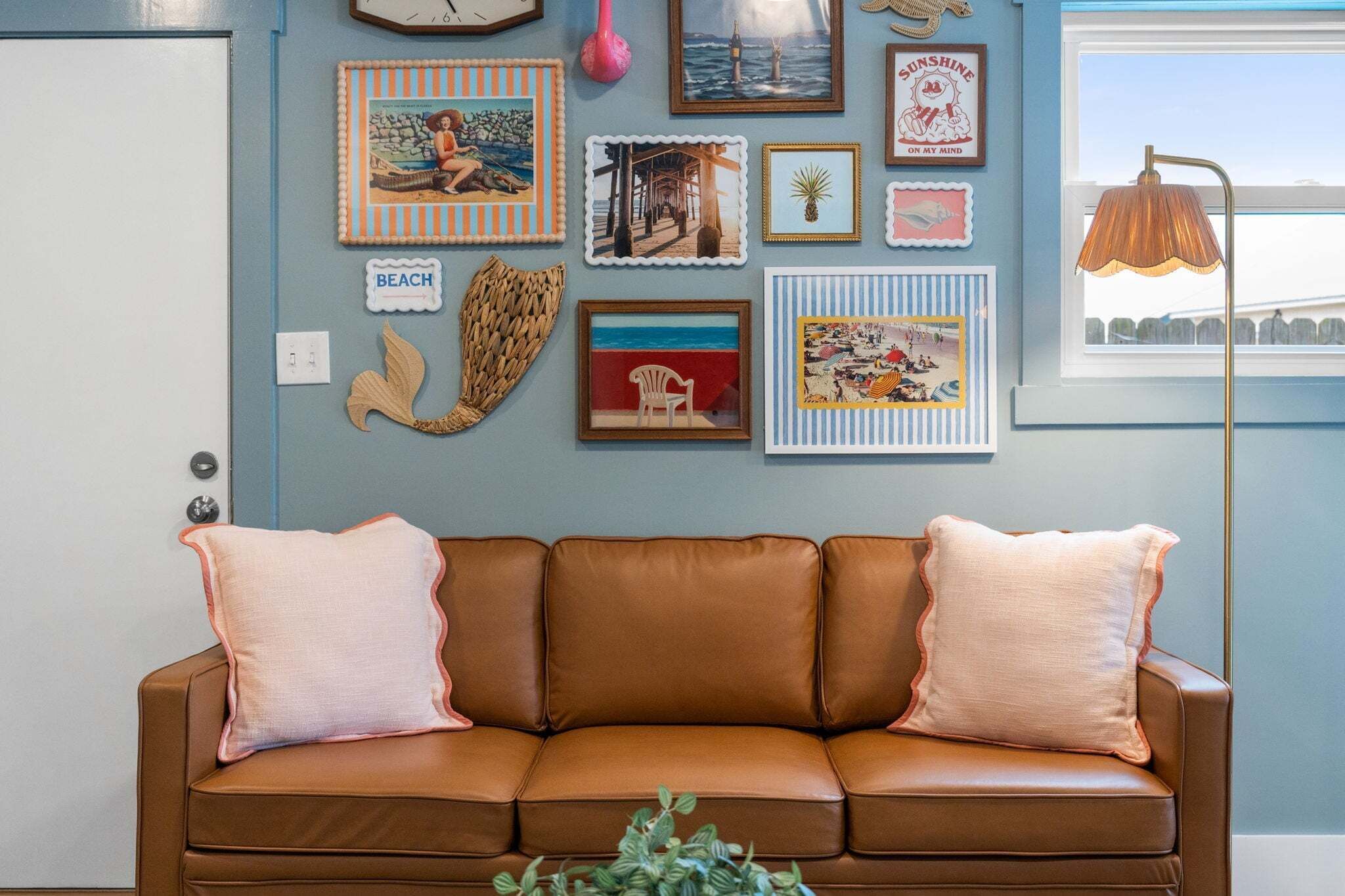 A brown leather sofa with two cushions, a wall decorated with various framed pictures, a clock, and a floor lamp.