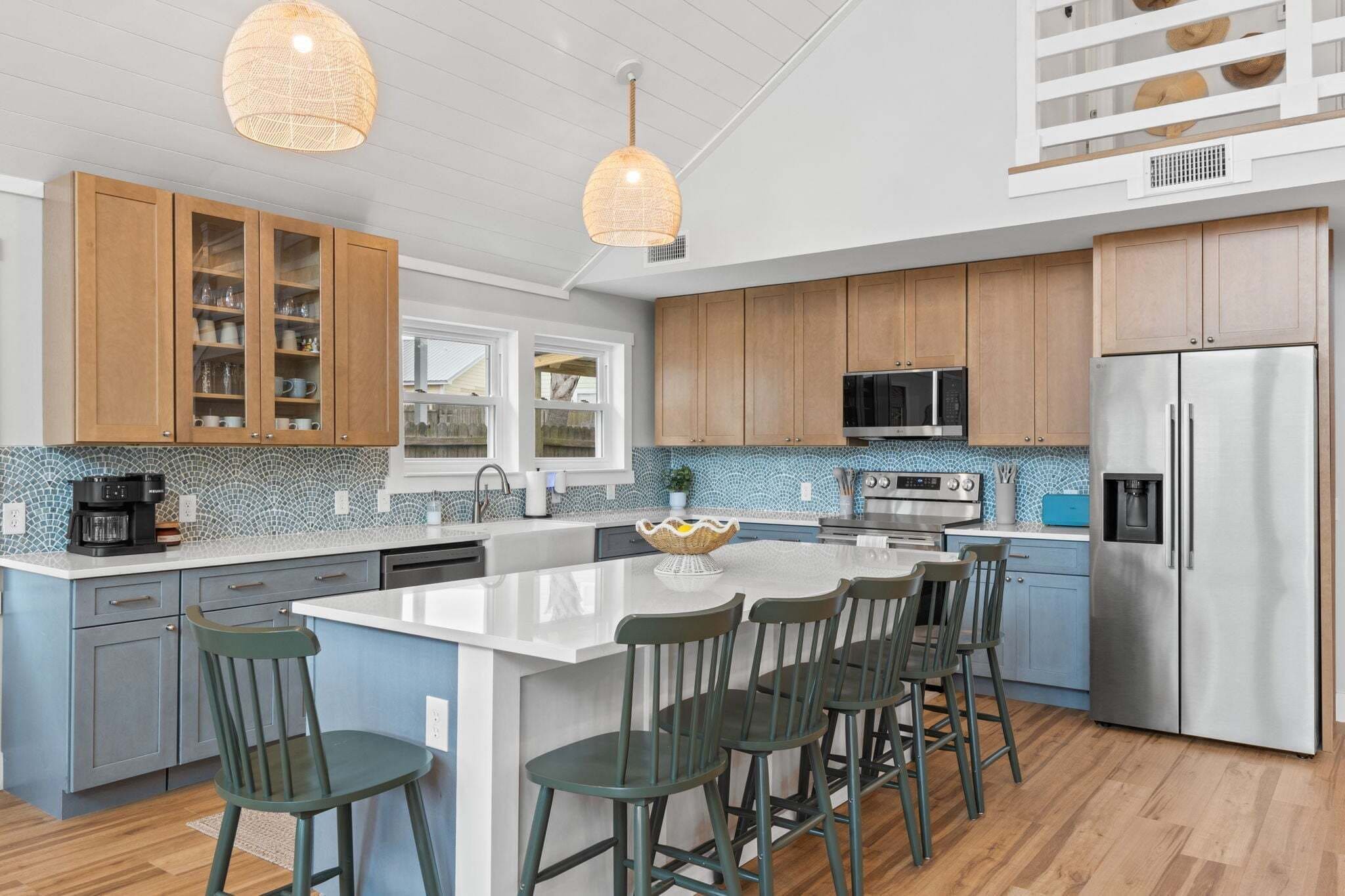 A modern kitchen with wooden cabinets, a large island with bar stools, stainless steel appliances, and a decorative hanging light.