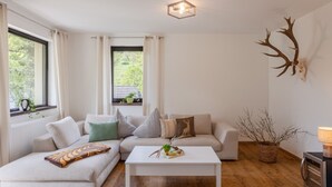 A modern living room with a sectional sofa, a white coffee table, a fireplace, and a large window with curtains. - Hunter's Lodge Adventure | Hot Tub I Wild Views (Gerolstein)