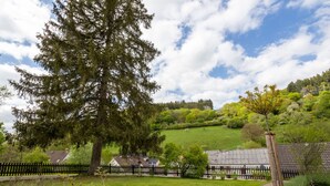 A rural landscape with a large tree, a fenced area, and a building with a tiled roof. - Hunter's Lodge Adventure | Hot Tub I Wild Views (Gerolstein)