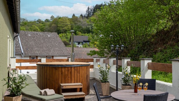 An outdoor patio with a hot tub, lounge chair, and table with chairs. - Hunter's Lodge Adventure | Hot Tub I Wild Views (Gerolstein)
