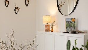 A room with a white cabinet, a lamp, a book, and wall-mounted deer antlers. - Hunter's Lodge Adventure | Hot Tub I Wild Views (Gerolstein)