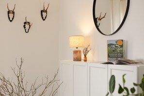 A room with a white cabinet, a lamp, a book, and wall-mounted deer antlers. - Hunter's Lodge Adventure | Hot Tub I Wild Views (Gerolstein)