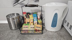 Una zona de cocina con cafetera, un colador de metal y un cesto de cápsulas de café.
