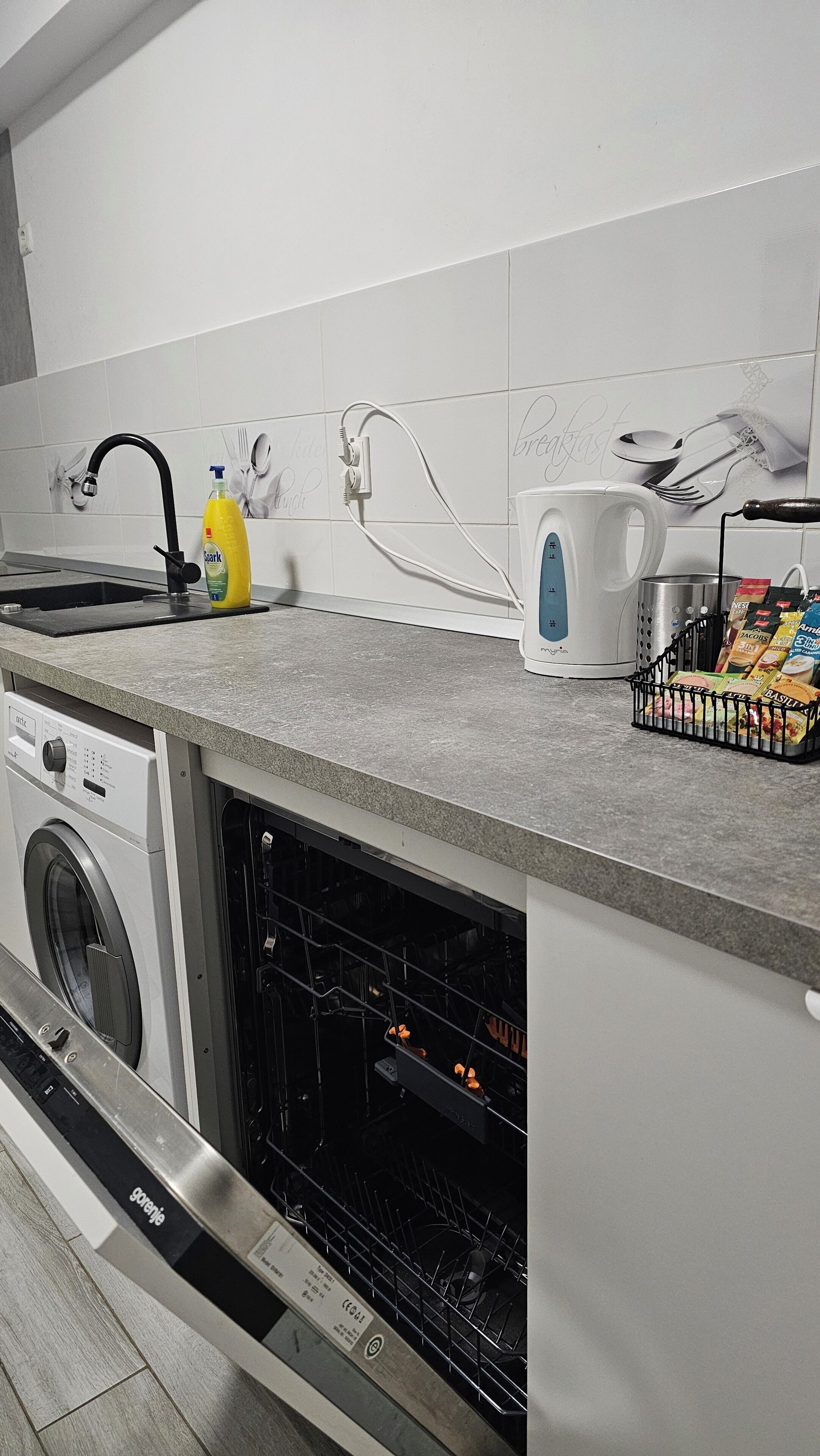 Une cuisine équipée d’un lave-linge, d’une machine à café et d’un égouttoir à vaisselle contenant des aliments.