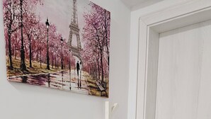 Huone, jossa on valkoinen ovi, valkoinen penkki, seinään kiinnitetty valaisin ja Eiffel-tornin kuva.