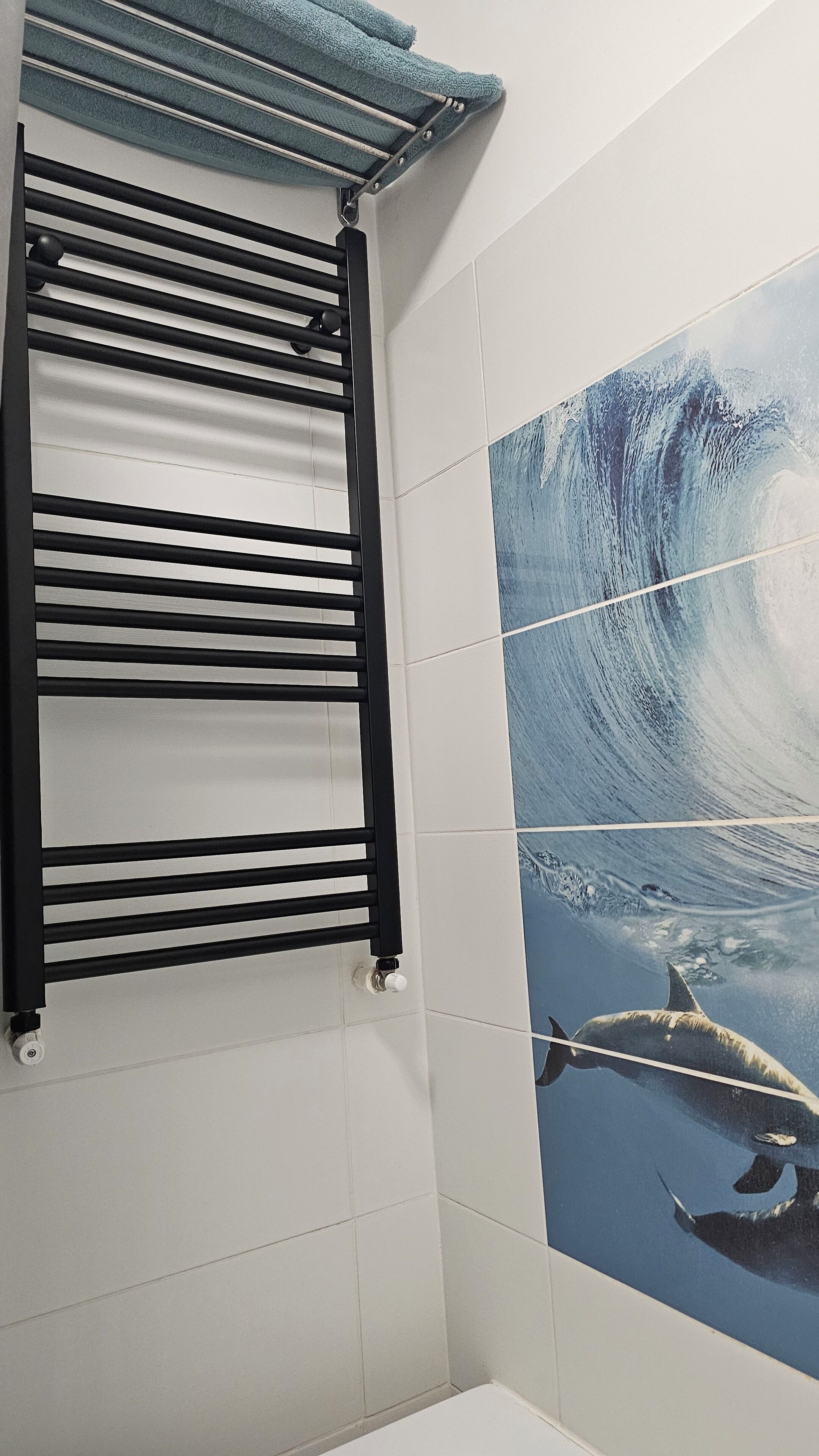 A bathroom with a black towel rack, white tiles, and a large wall mural of a whale.