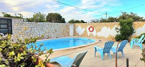 A swimming pool with a stone wall, blue chairs, and a lifebuoy. - Apartment Oceano - Sun and salt with terrace and saltwater pool (Moncarapacho)