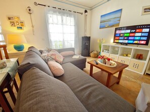 A living room with a sofa, a coffee table with a vase, a television, and a bookshelf. - Apartment Oceano - Sun and salt with terrace and saltwater pool (Moncarapacho)