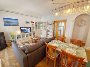 A living room with a sofa, dining table set for four, a TV, and a bookshelf. - Apartment Oceano - Sun and salt with terrace and saltwater pool (Moncarapacho)