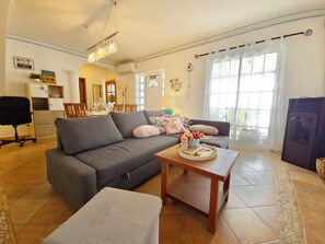 A living room with a sofa, ottoman, coffee table, and a dining area with chairs and a table. - Apartment Oceano - Sun and salt with terrace and saltwater pool (Moncarapacho)