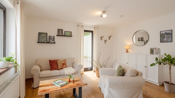 Ein Wohnzimmer mit einer Couch, einem Couchtisch und einem Kamin. An den Wänden hängen Bilder in Rahmen und über der Couch befindet sich ein Spiegel.