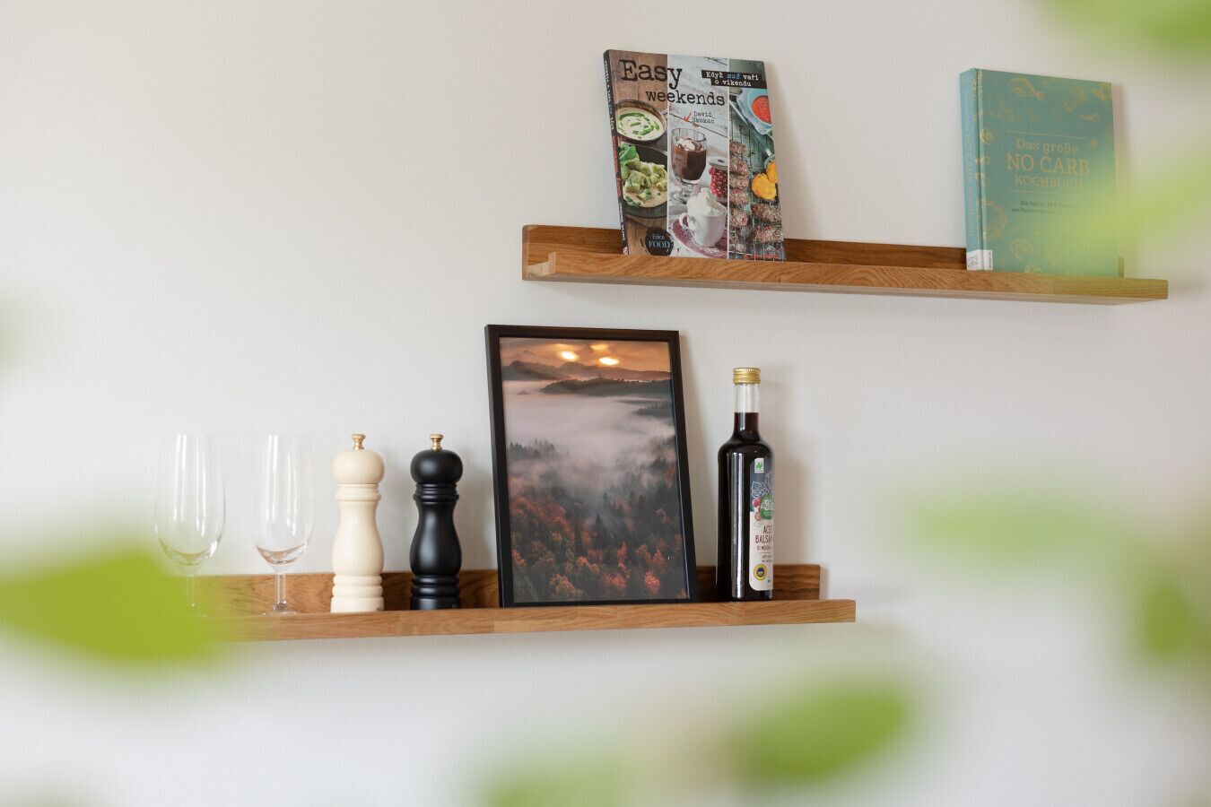 Zwei Holzregale mit Büchern, einem gerahmten Bild, Salz- und Pfefferstreuern und einer Weinflasche.