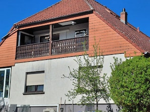 Una casa de dos pisos con techo de tejas rojas, un balcón con barandilla metálica y una pared exterior blanca.