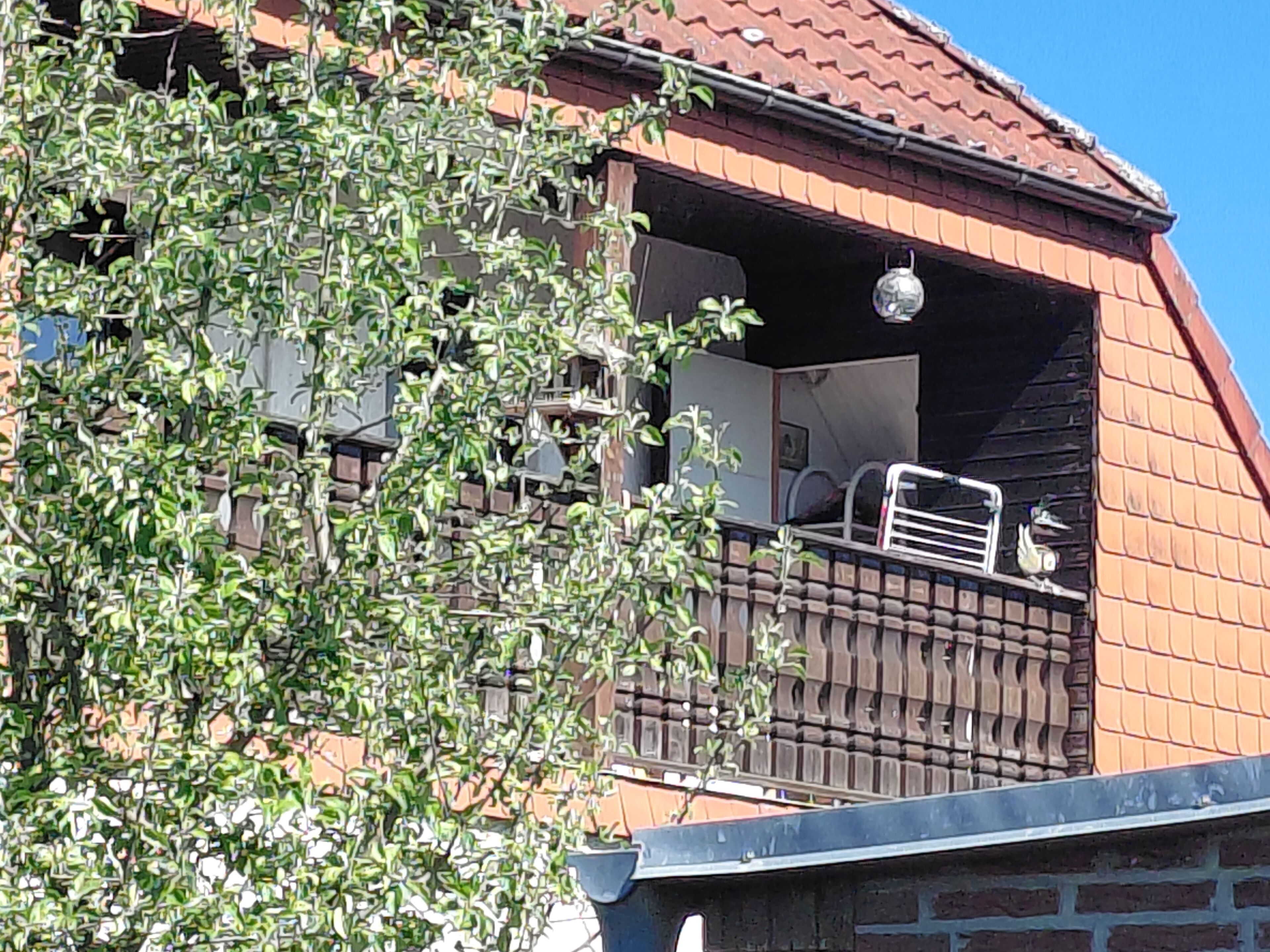 A building with a red-tiled roof, a balcony with a metal railing, and a window with a decorative element.