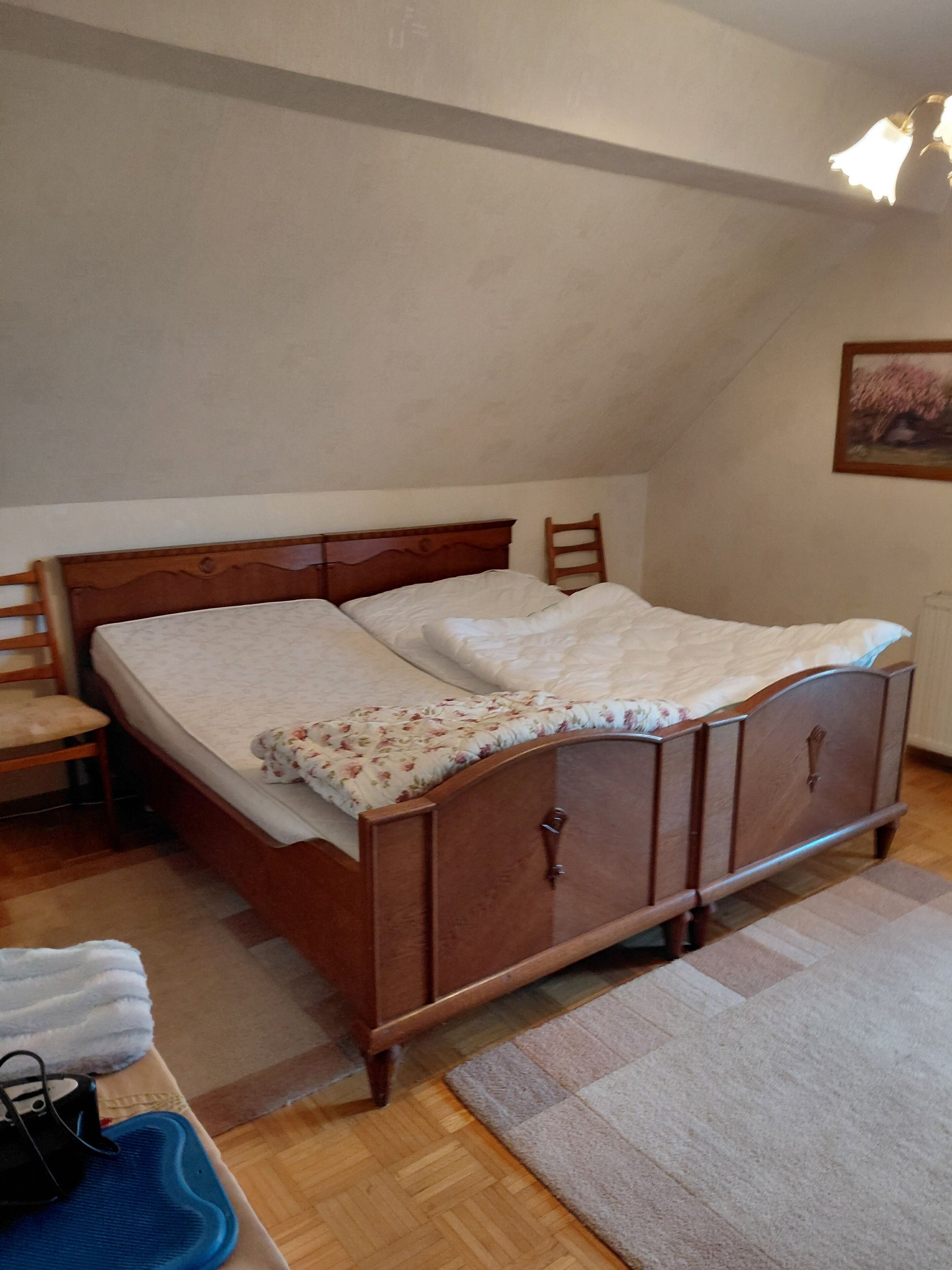 A bedroom with a wooden bed, a chair, a small table, and a painting on the wall.