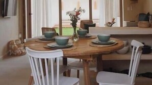 Uma sala de jantar com mesa redonda, cadeiras brancas e vista através de grandes janelas.
