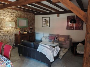 A cozy living room with a stone wall, wooden beams, a sofa, a coffee table, and a fireplace. - Gîte, heated swimming pool in Hunawihr, Ribeauvillé and Colmar on the Wine Route (Hunawihr)