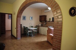 Ein Essbereich mit einer Ziegelbogenarchitektur, einem Tisch mit Stühlen und einer Küche im Hintergrund.