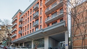 Un edificio de ladrillo de varios pisos con balcones, un acceso cubierto y coches estacionados.