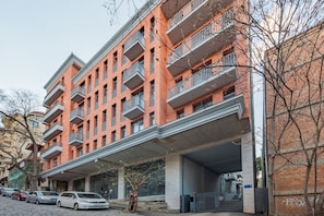A multi-story brick building with balconies, a covered entrance, and parked cars. - HB apartments Chitadze (Tbilisi)