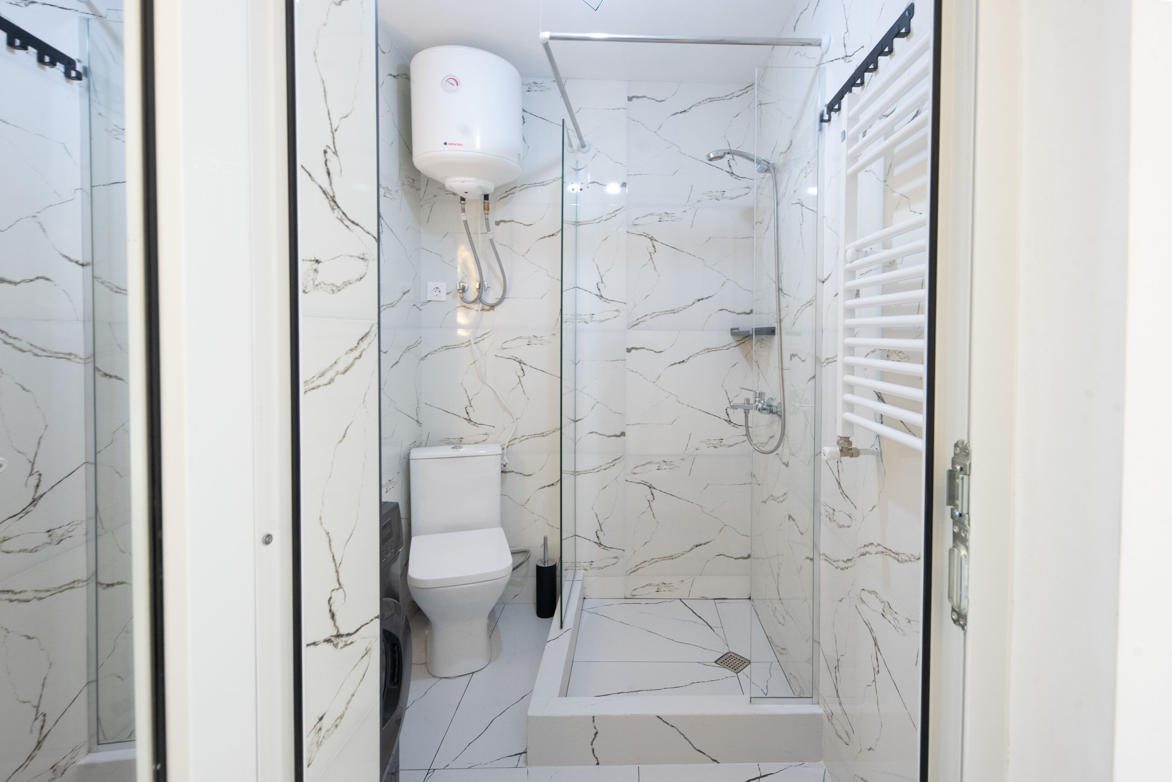 A bathroom with a glass-enclosed shower, a toilet, and a white marble floor.
