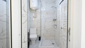 A bathroom with a glass-enclosed shower, a toilet, and a white marble floor.